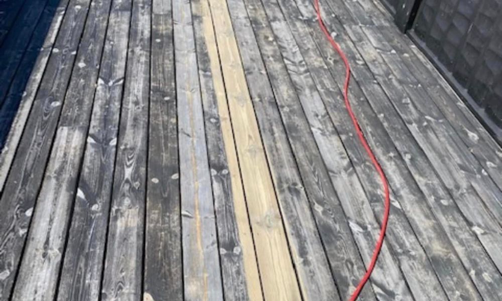 Bilde av en delvis rengjort terrasse. Kontrast mellom gamle, grå treplanker og nylig rengjorte, lyse planker er tydelig. En rød strømkabel ligger på terrassen.