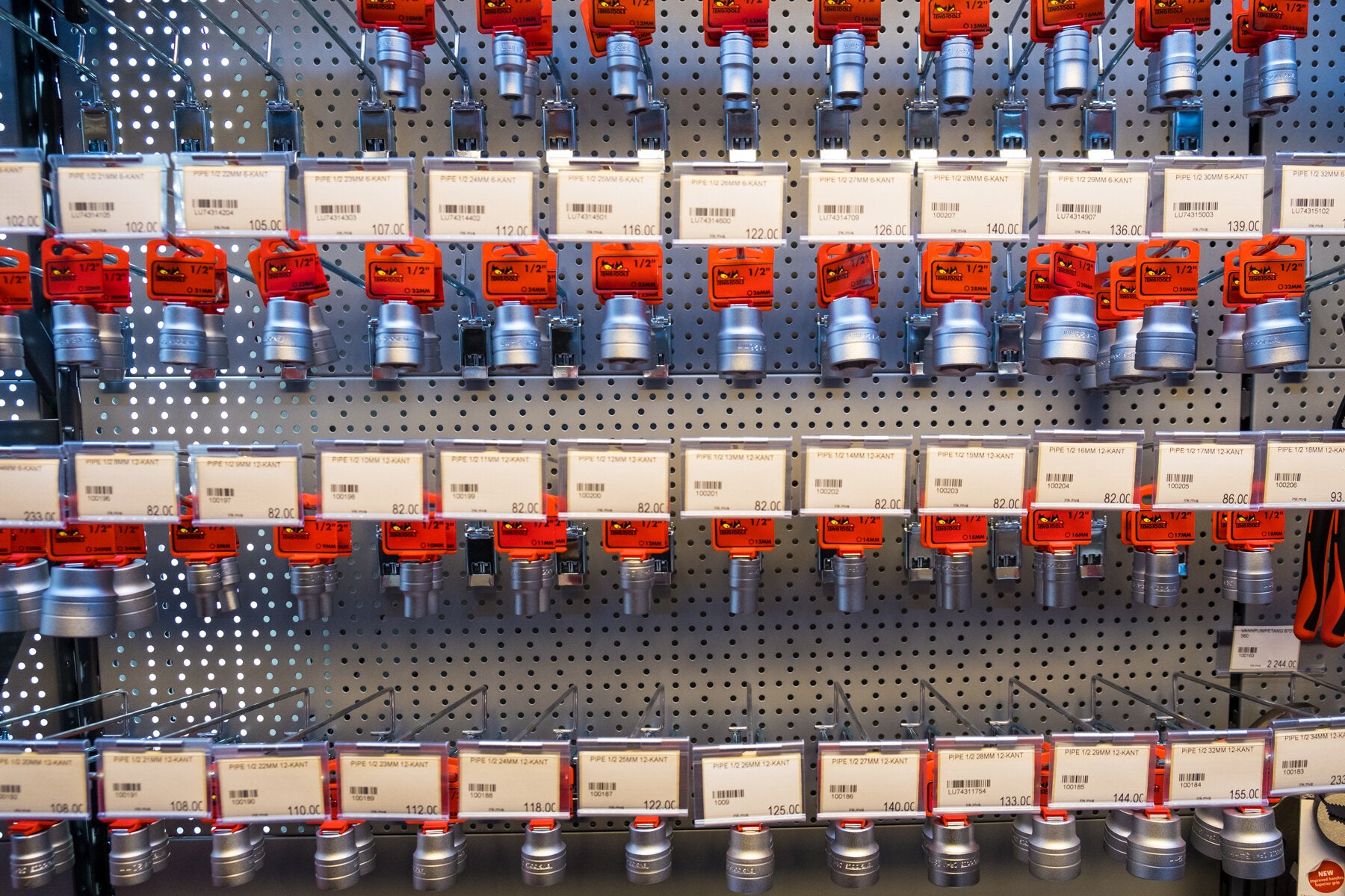 Et bilde av et godt organisert utvalg av rørkoblinger og tilbehør på en butikkhylle, med tydelige priser og størrelser vist på etikettene.
