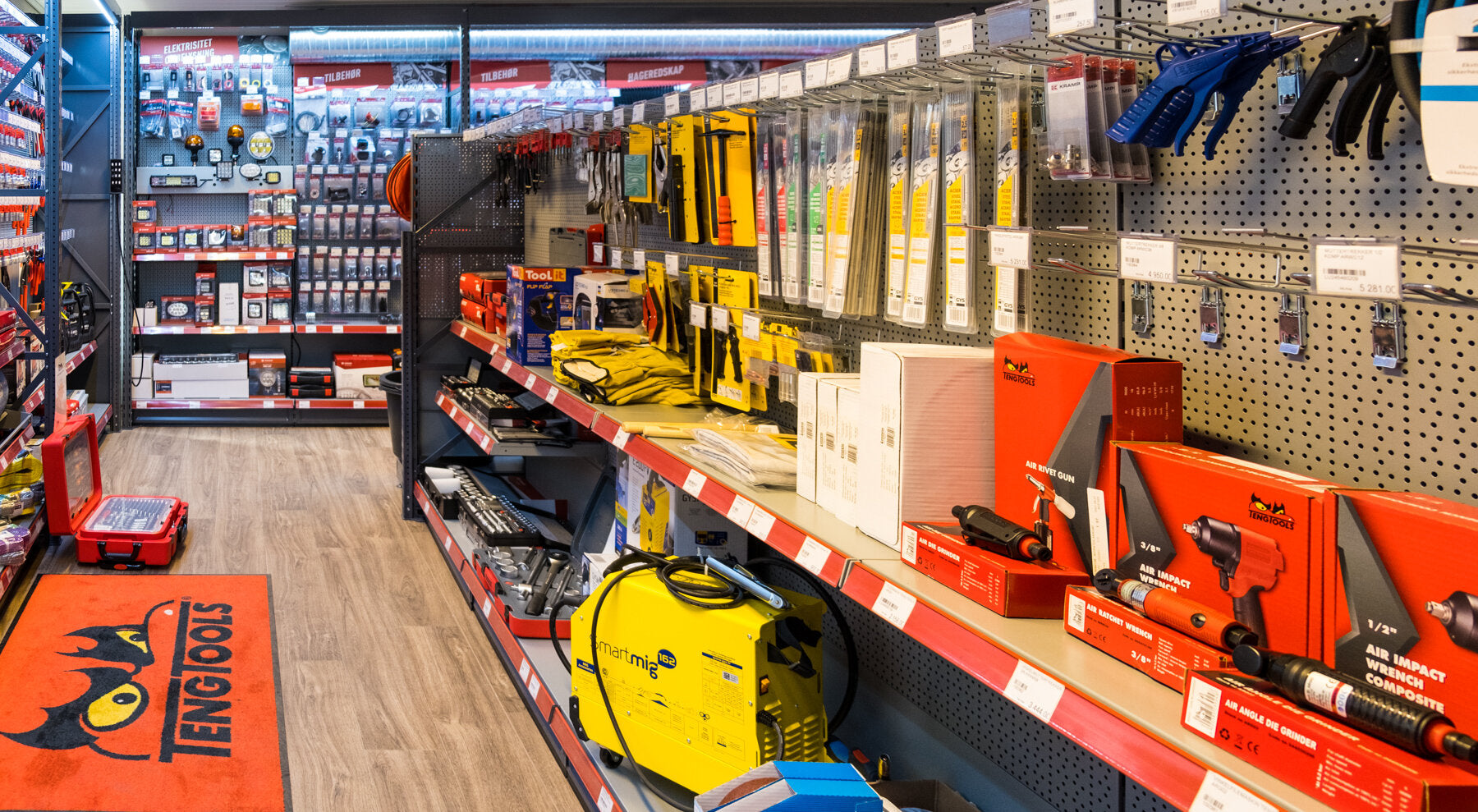 En verktøybutikk med et bredt utvalg av håndverktøy, elektrikertilbehør og luftverktøy, alle pent organisert på hyller og display i en ryddig gangvei.