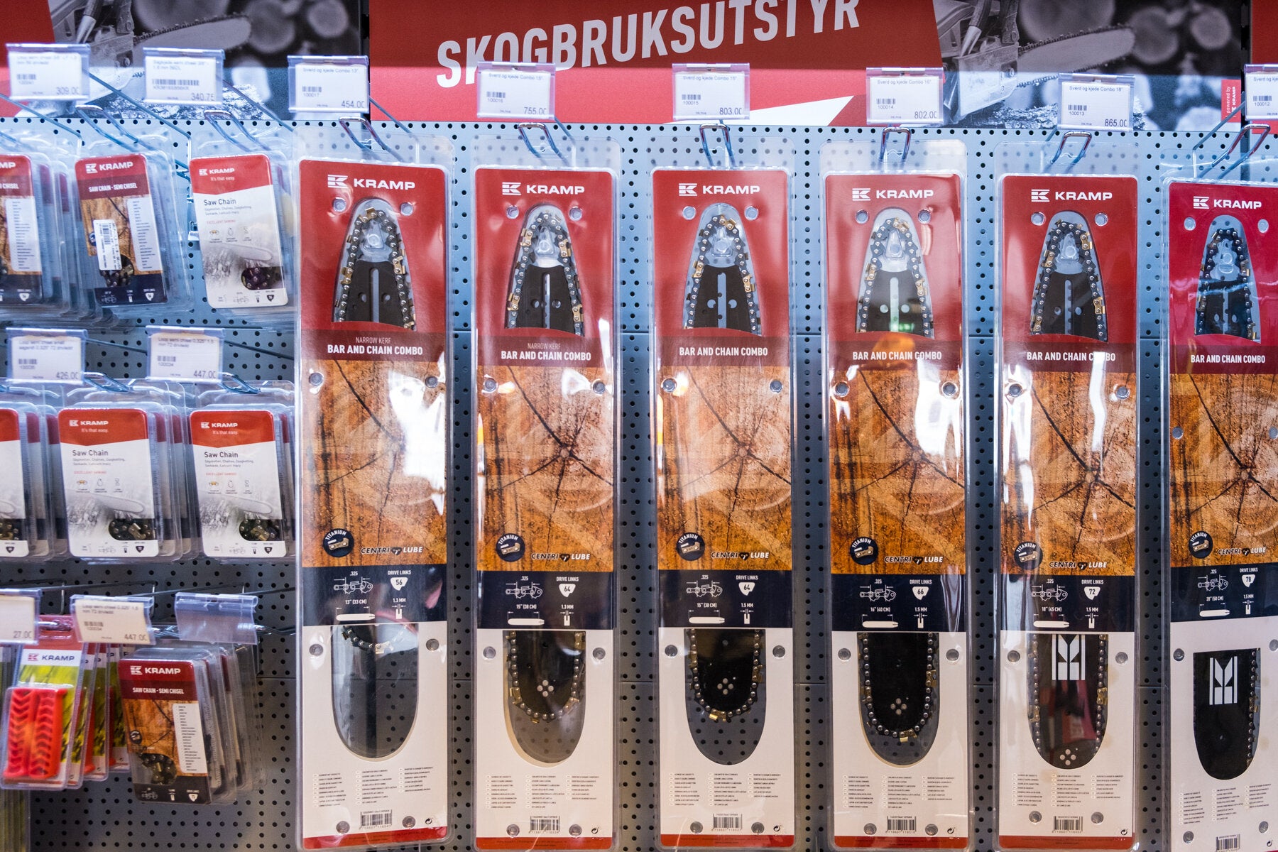 Hyller i en butikk fylt med skogbruksutstyr, inkludert motorsagsverd og sagkjeder, alle organisert i pakker klare til salg.