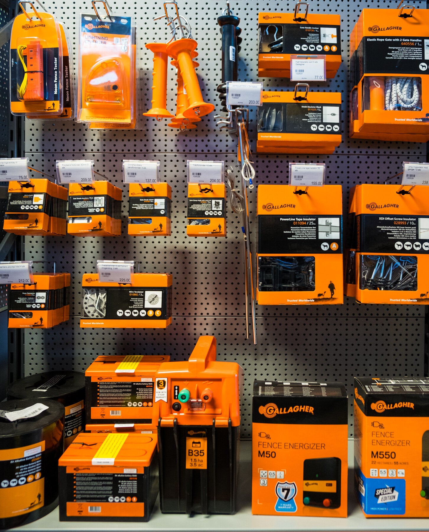 Hylle med Gallagher gjerdeutstyr, inkludert isolatorer, strømgjerdeapparater og tilbehør. Produktene er pakket i oransje esker og er tydelig merket.