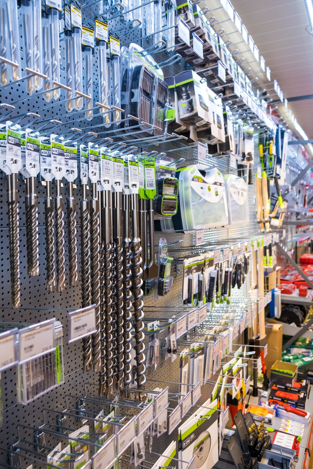 En vegg med et bredt utvalg av bor, kniver og annet verktøy til salgs hos NHM Utstyr. Produktene er tydelig merket og organisert for enkel tilgang.