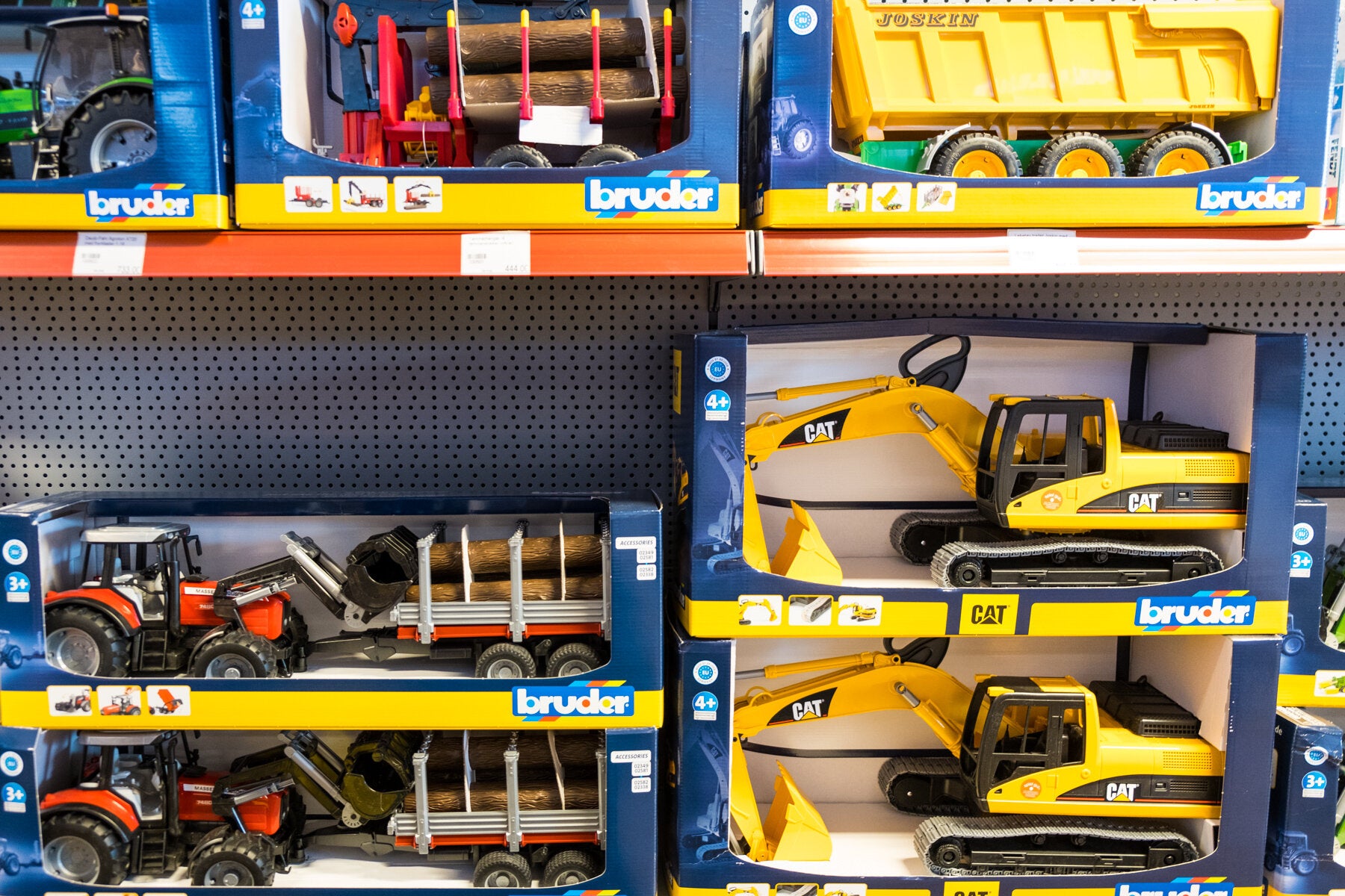 Hylle med Bruder lekebiler, inkludert lastebiler, traktorer og gravemaskiner i esker. Passer for barn fra 3 år og oppover, med realistiske detaljer og funksjoner.