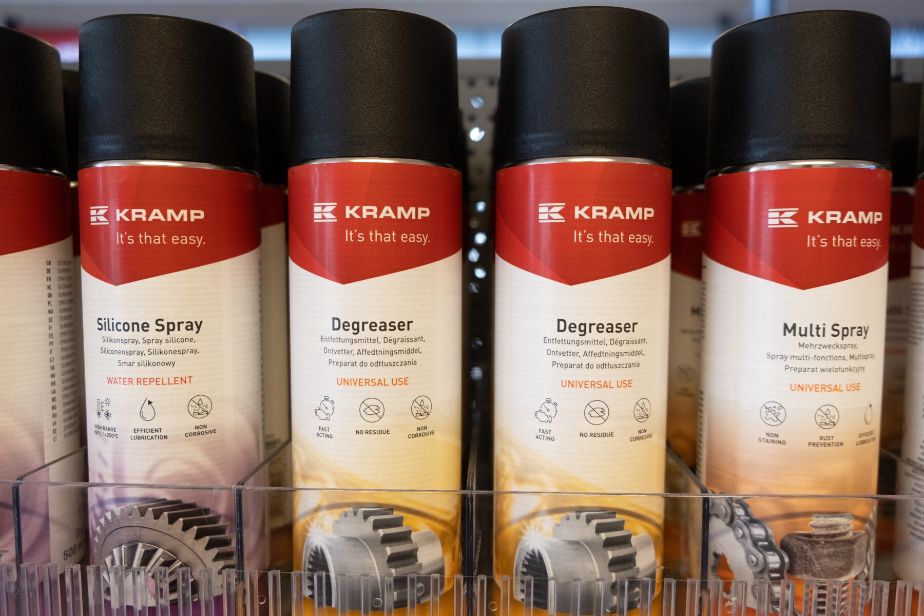 Kramp-produkter på en hylle: silikonspray, avfettingsmiddel og multispray, tydelig merket for universell bruk og deres spesifikke fordeler.